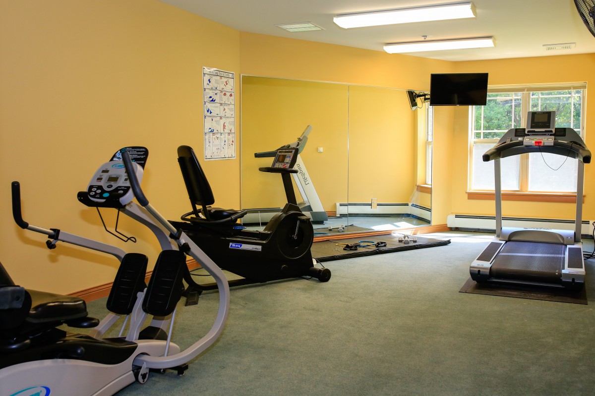 A small gym with exercise equipment including a treadmill, elliptical machine, and a TV on the wall.