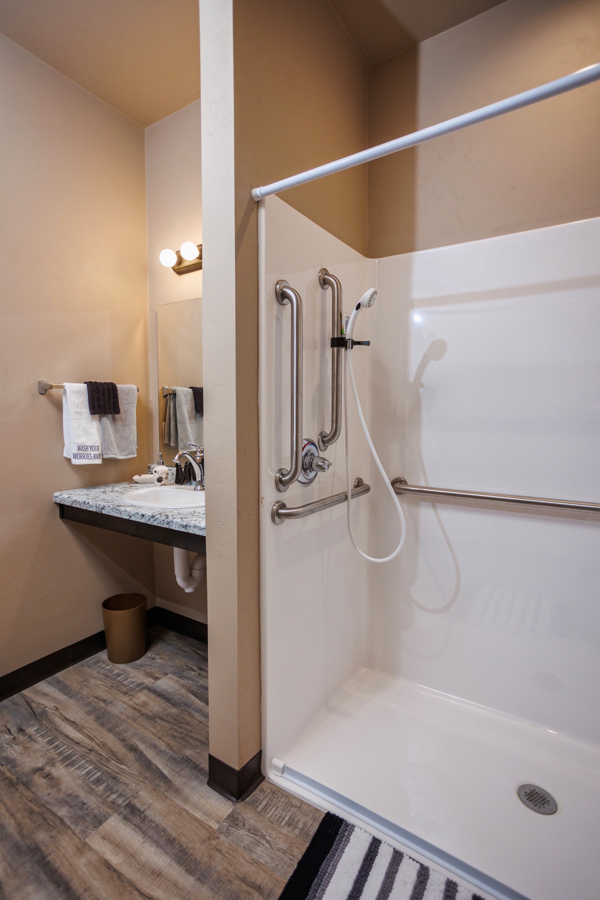 An accessible bathroom featuring a walk-in shower with grab bars and a nearby sink with a mirror.