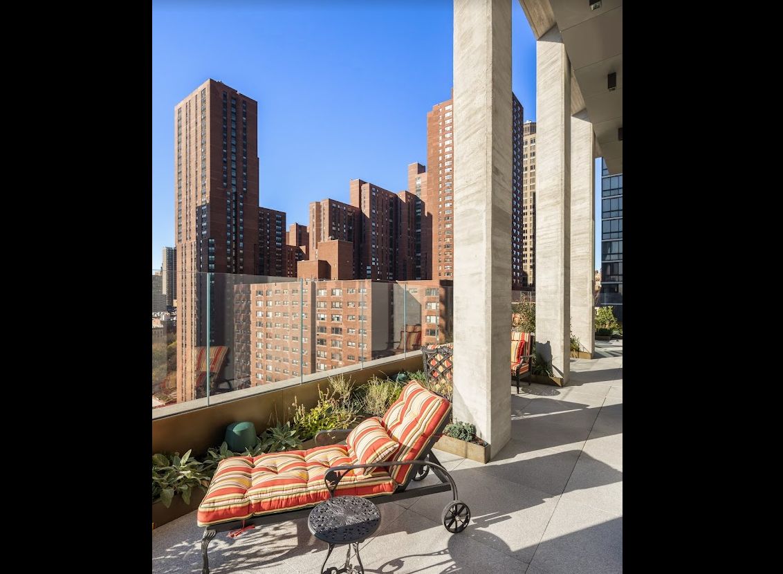 A sunny balcony with a chaise longue overlooking a cityscape of tall buildings.