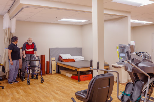 A spacious rehabilitation room equipped for elderly care, featuring a bed and supportive medical equipment.