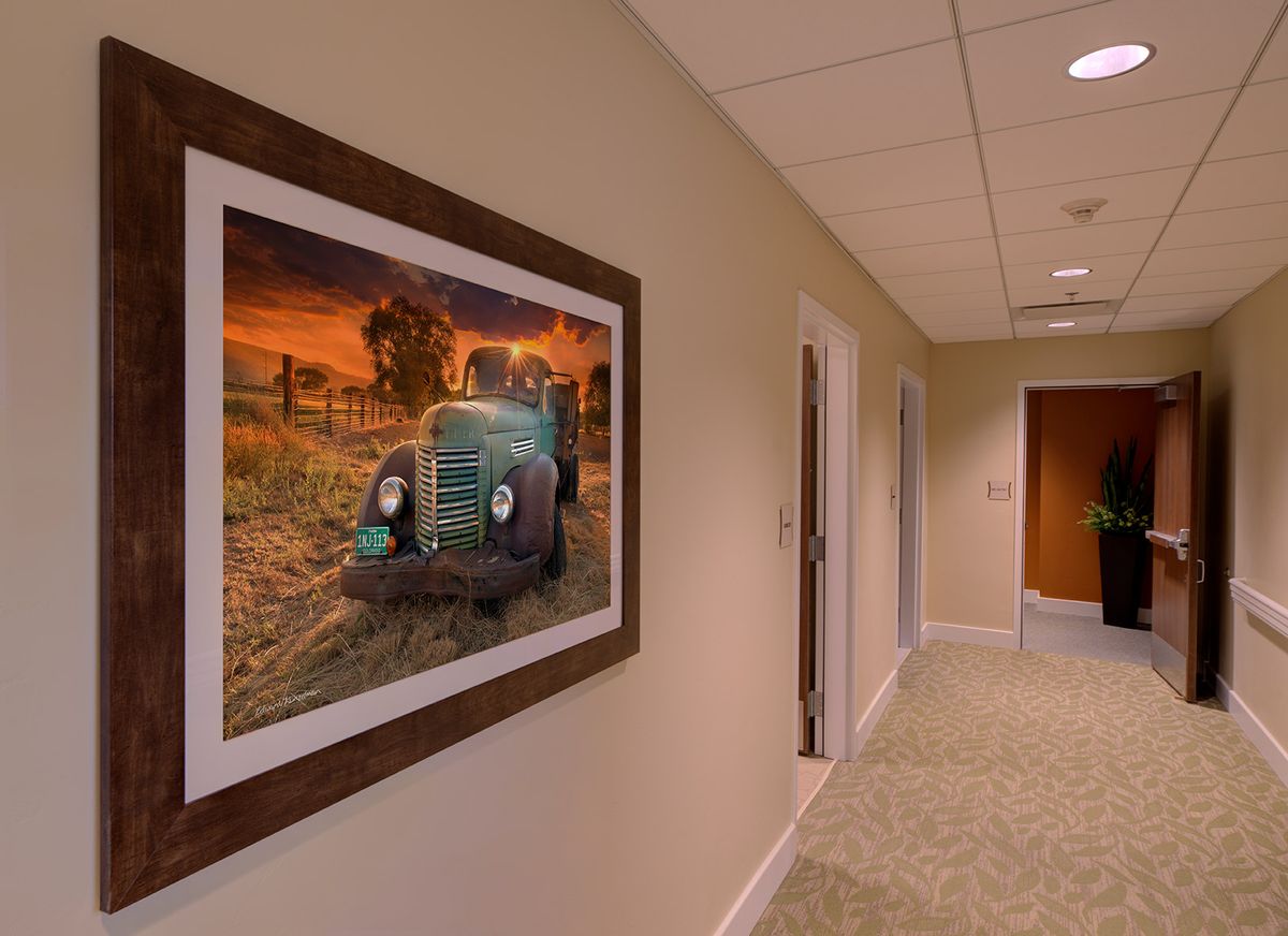 A hallway with a framed painting of an old tractor at sunset on the wall.