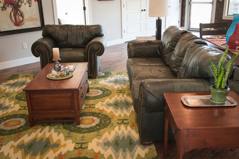 A cozy living room with a sofa, armchair, wooden coffee tables, and a patterned rug.