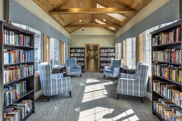 A cozy library seating area with comfortable chairs and ample natural light streaming through large windows.