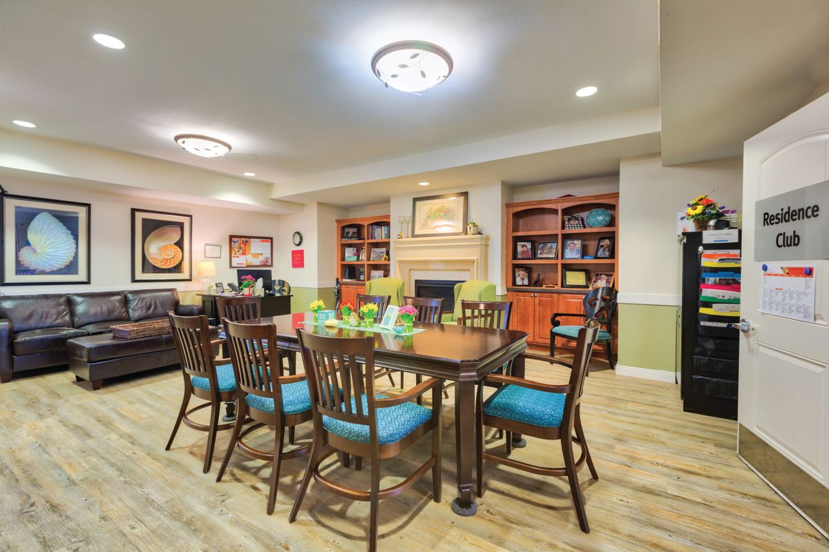 A cozy dining area featuring a central table surrounded by chairs, with bookshelves, artwork, and a fireplace enhancing the ambiance.