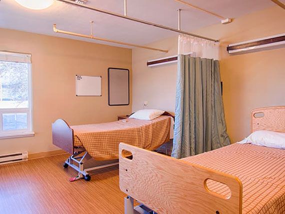 An empty hospital room with two beds and a privacy curtain.