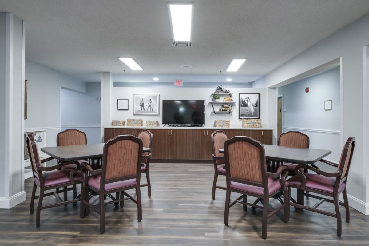 A spacious meeting room with tables and chairs, featuring artwork on the walls and a large television.
