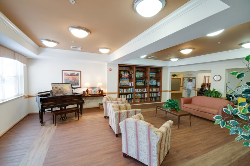 A cozy lobby with a seating area, piano, and bookshelves.