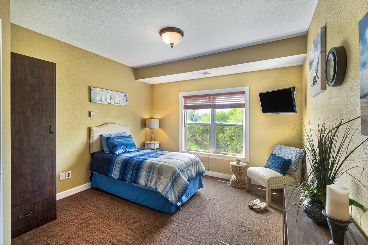 A cozy bedroom with a single bed, window view, and a wall-mounted television.