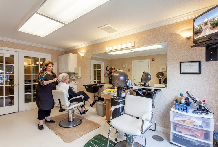 A cozy hair salon with a hairdresser attending to a customer, surrounded by chairs and salon equipment.