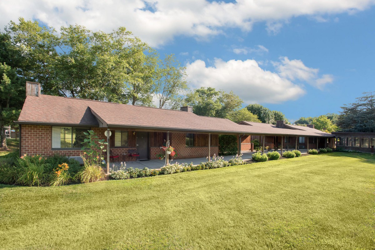 A long brick house with a well-maintained lawn under a partly cloudy sky.