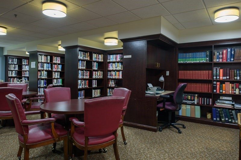A quiet library space with bookshelves, a round table with chairs, and a small desk for studying.