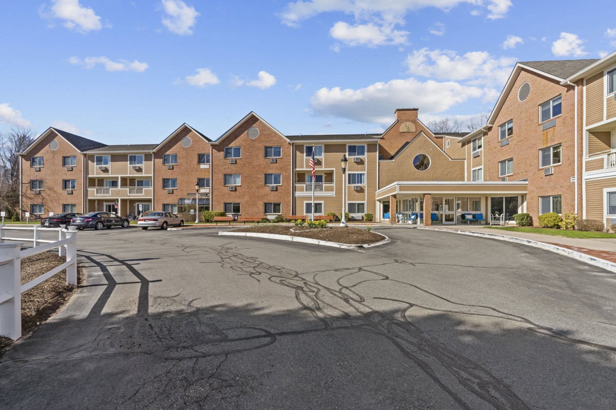 A hotel exterior with a spacious parking lot under a partly cloudy sky.
