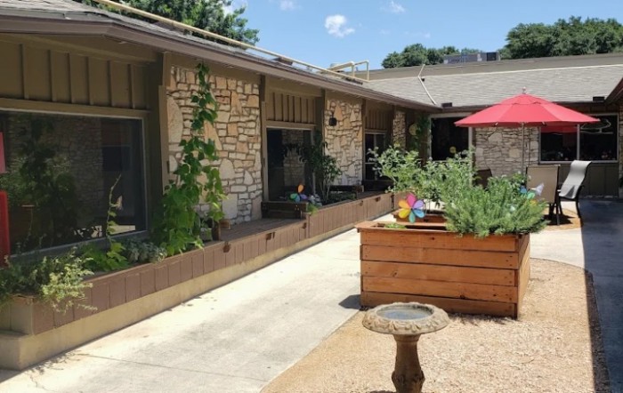A sunny patio with stone walls, raised planter boxes, and a red umbrella.