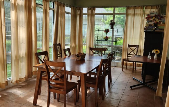 A cozy dining room with wooden furniture and large windows letting in natural light.