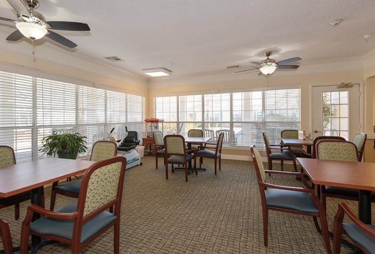 A cozy dining area with multiple tables and chairs, surrounded by large windows and equipped with ceiling fans.