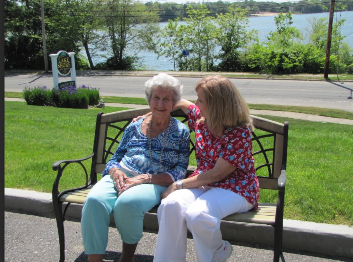 Two individuals sitting on a bench by the lake, enjoying a sunny day.