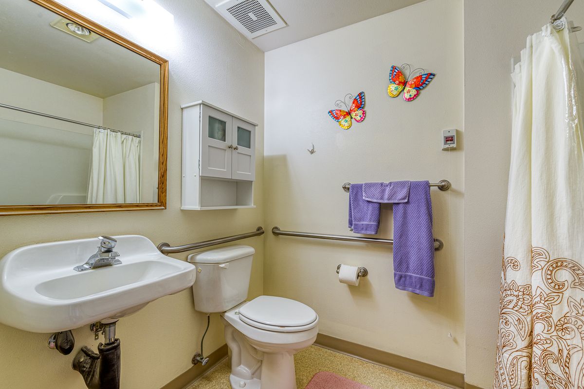 A bright bathroom with butterfly wall decals and a purple towel hanging on a handrail.