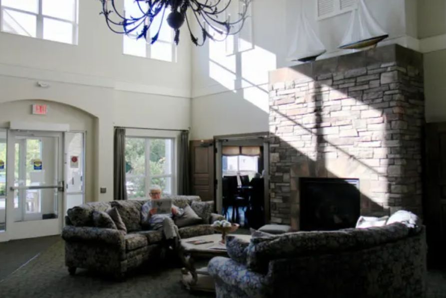 A spacious living room with high ceilings, featuring a chandelier, large windows, a stone fireplace, and comfortable sofas.