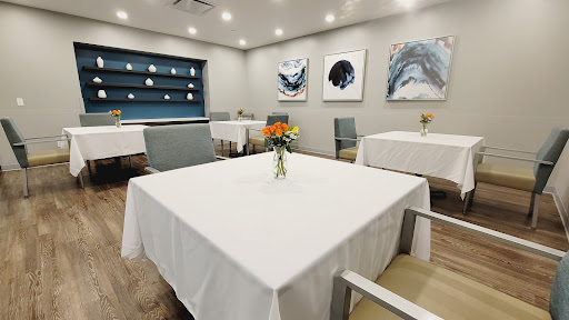 A neatly arranged dining area featuring white tablecloths, floral centerpieces, and contemporary artwork.