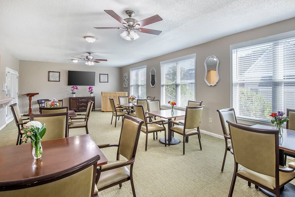 A bright dining room with several tables and chairs, ceiling fans, and large windows.