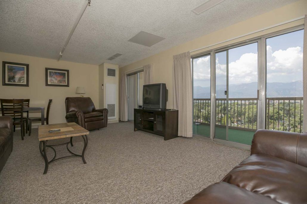 A cozy living room with leather furniture, a television, and a balcony offering a scenic view.