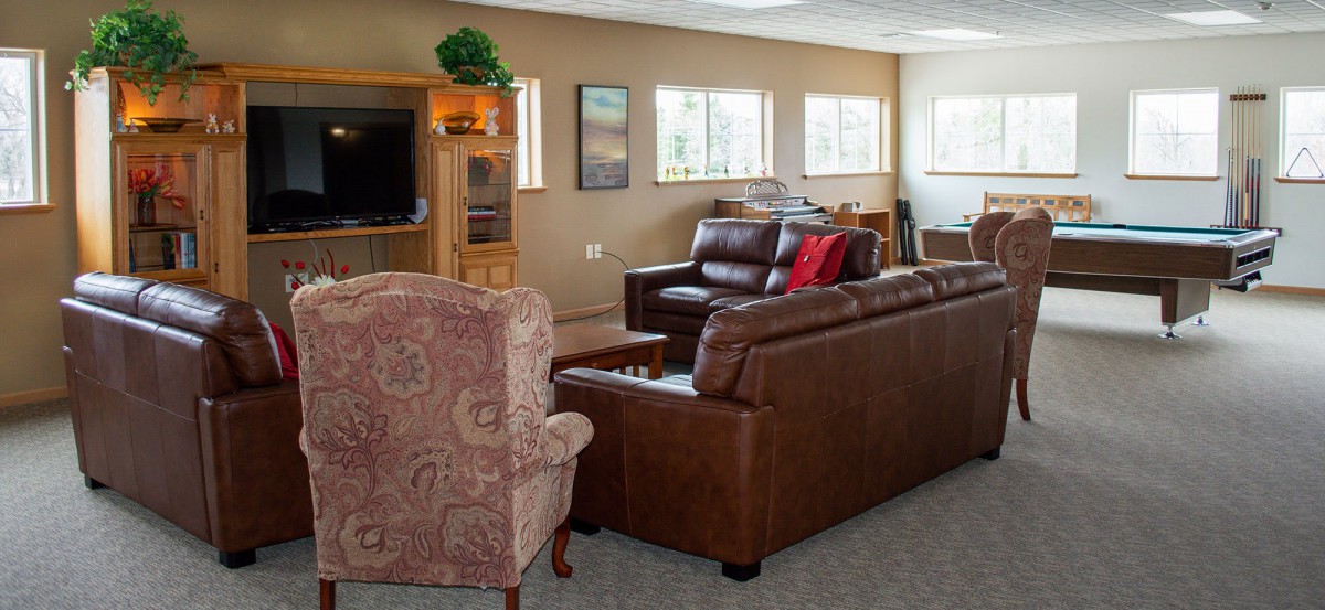 A cozy living room with comfortable leather sofas, a patterned armchair, and a wooden cabinet housing a television.