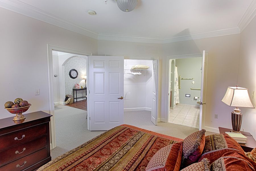 A cozy bedroom with an open layout, featuring a patterned bedspread and neutral walls.