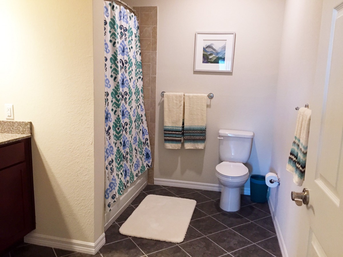 A clean and organized bathroom featuring a shower with a colorful curtain, a toilet, and neatly arranged towels.