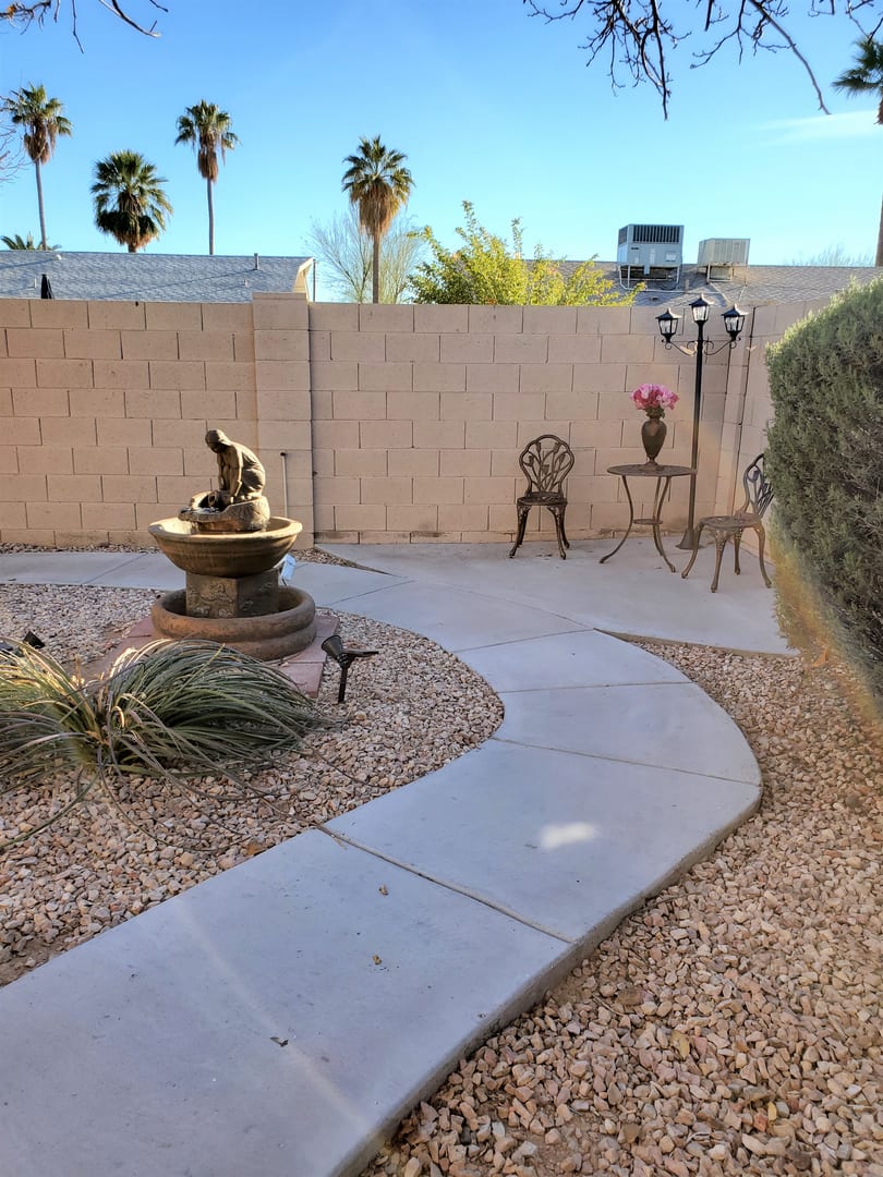 A peaceful garden patio featuring a decorative fountain and seating area with palm trees in the background.