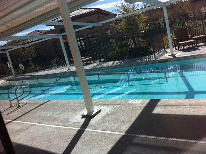 An outdoor swimming pool with surrounding buildings and clear blue water under a sunny sky.