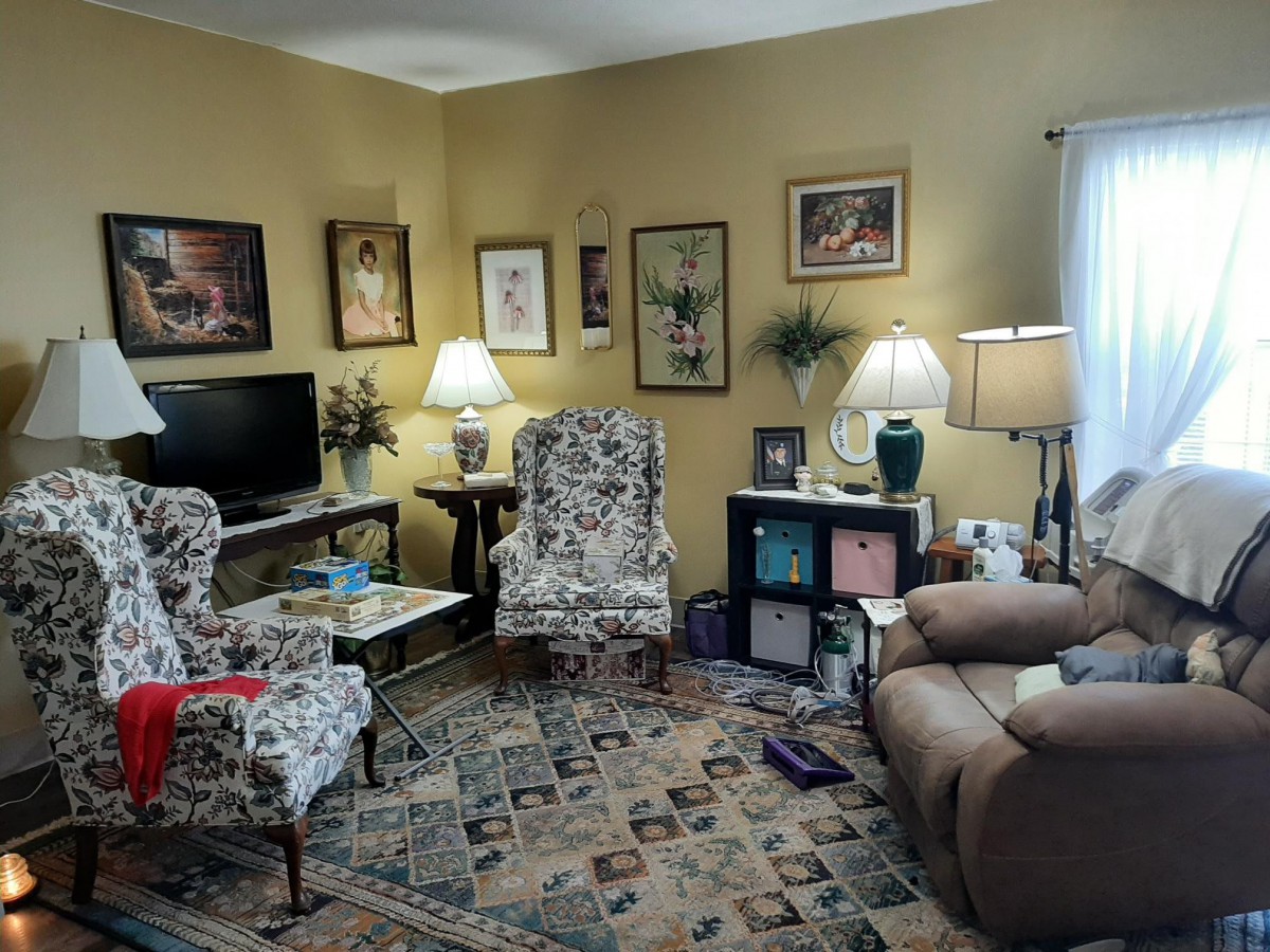 A cozy living room with various artworks on the walls, two patterned chairs, a sofa, and a television.