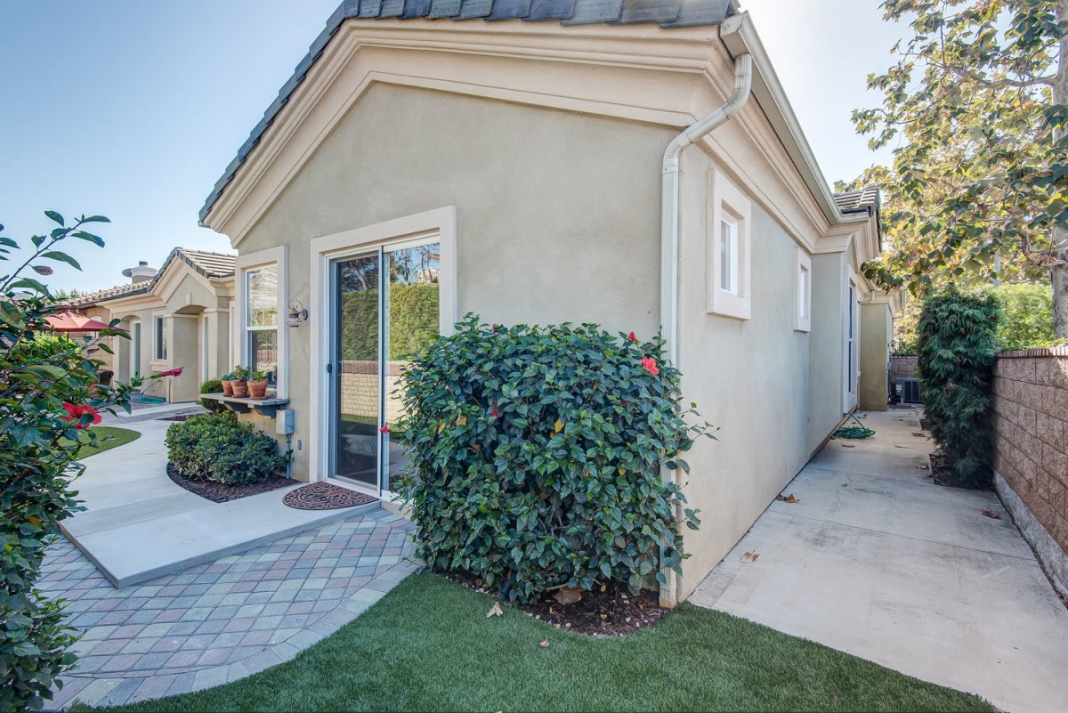 A small house exterior with a neatly landscaped yard and bushes along a pathway.
