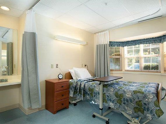 A well-lit hospital room with a single bed, nightstand, and window.