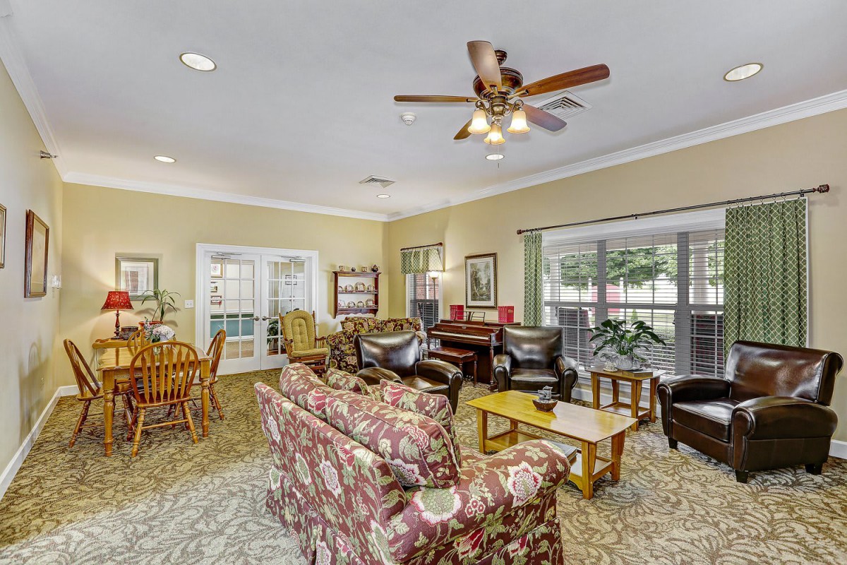 A cozy living room with a ceiling fan, sofas, and large windows.