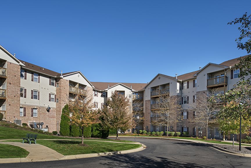 A suburban apartment complex with landscaped surroundings under a clear blue sky.