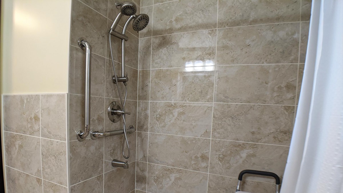 A modern shower with tiled walls and grab bars for accessibility.