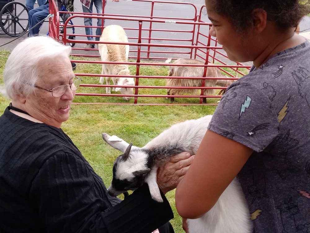 Two people enjoying time with a goat at a petting zoo.