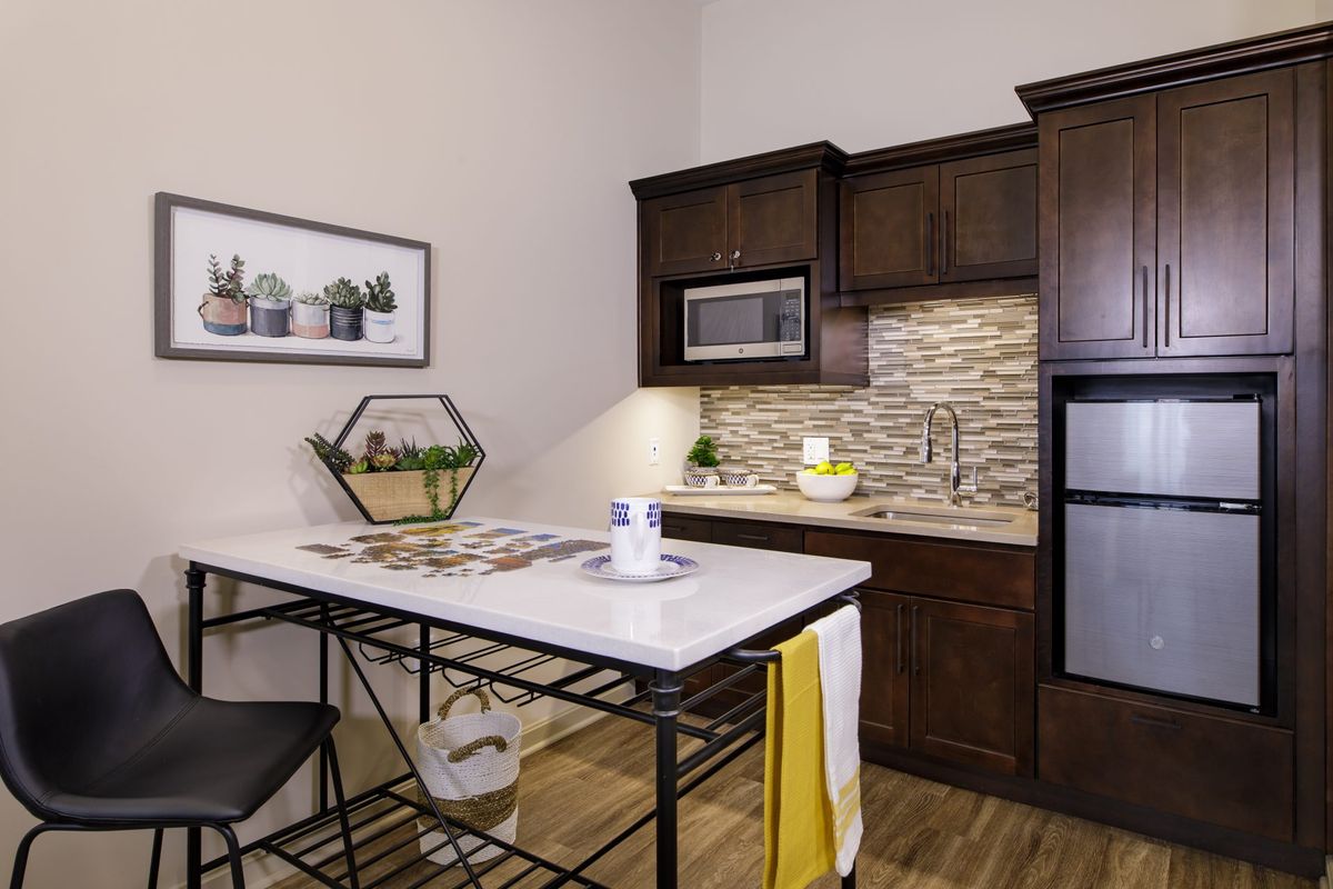 A modern kitchen with dark cabinetry, a small dining table, and various appliances.