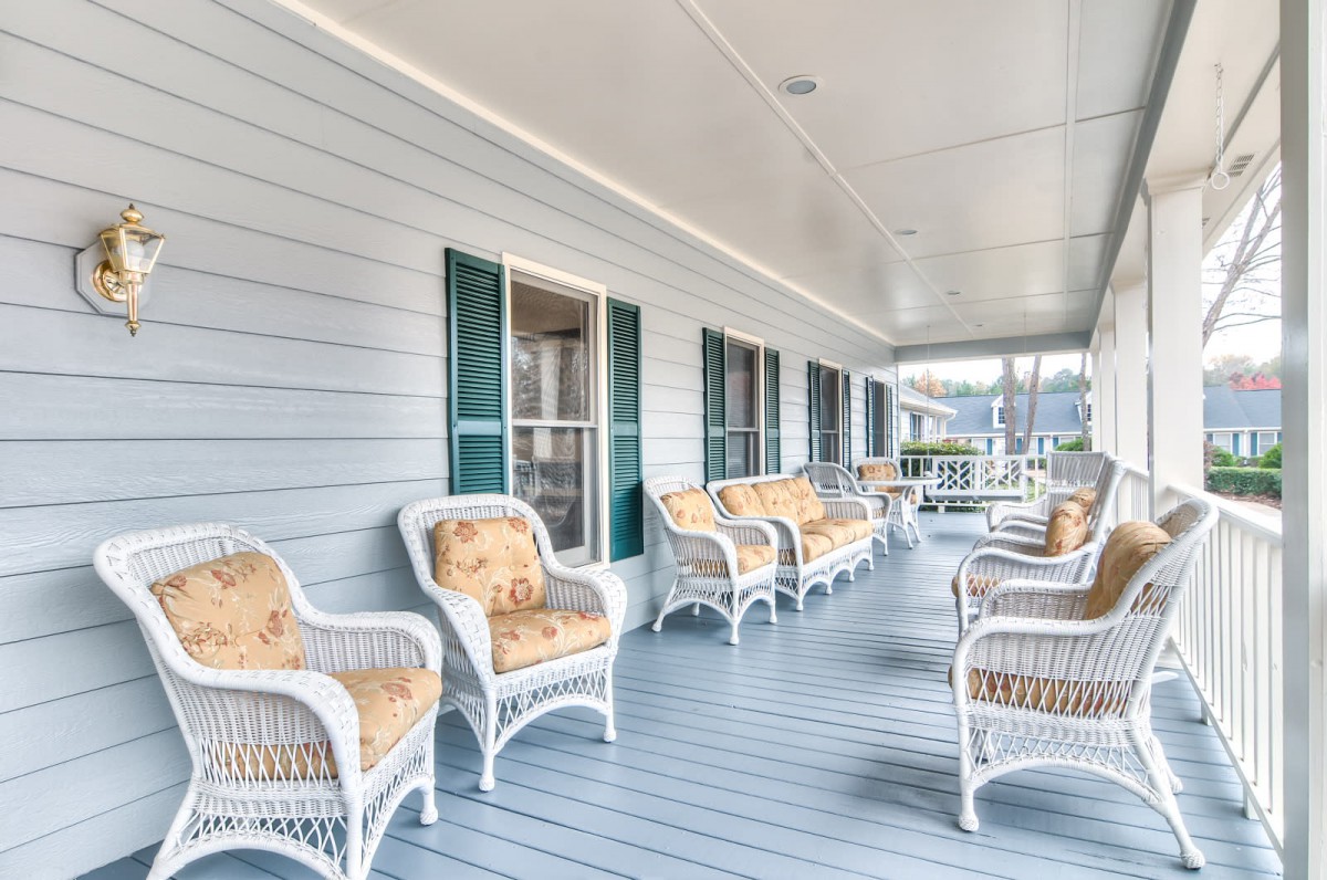 A view of a spacious porch with wicker chairs and cushions, offering a comfortable outdoor seating area.