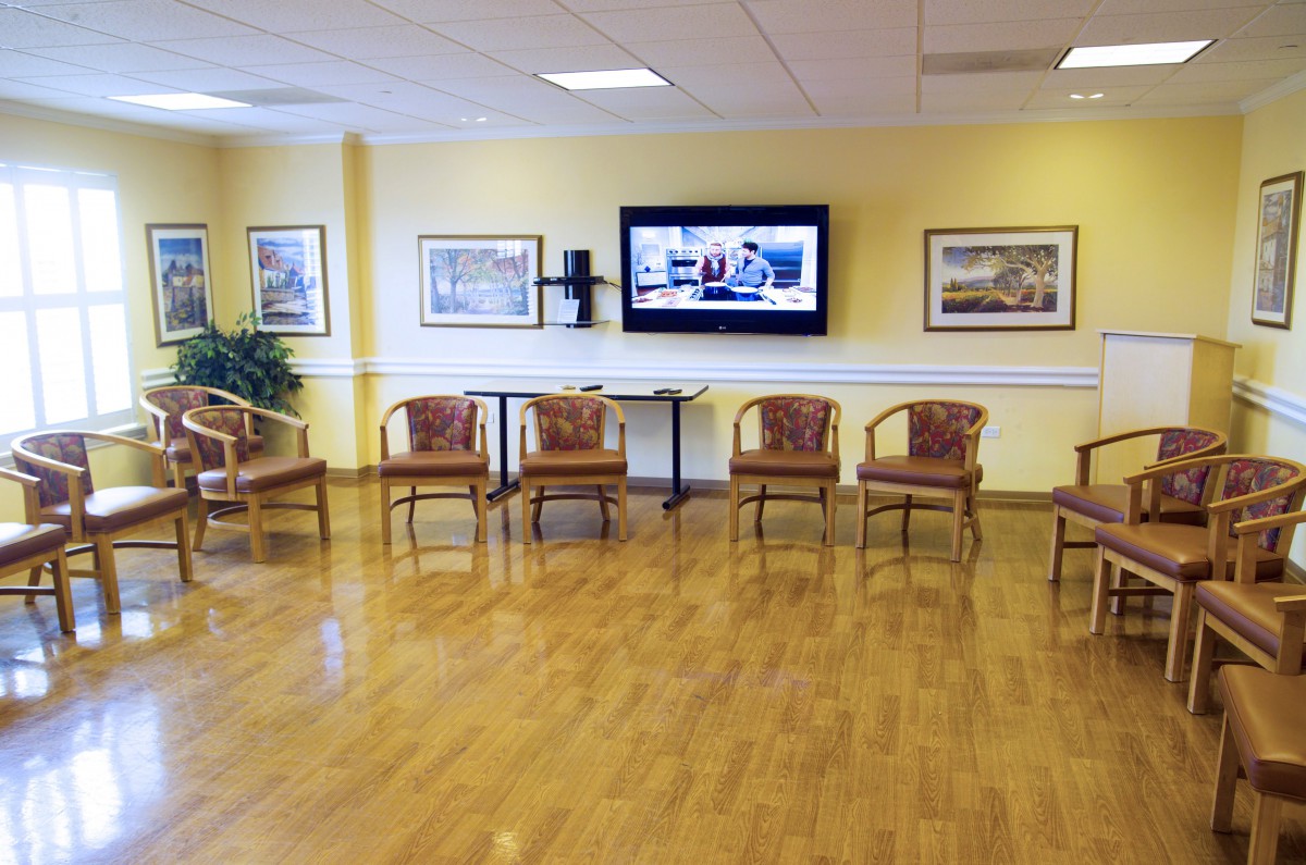 An empty waiting room with chairs lined against a wall and a television mounted above.