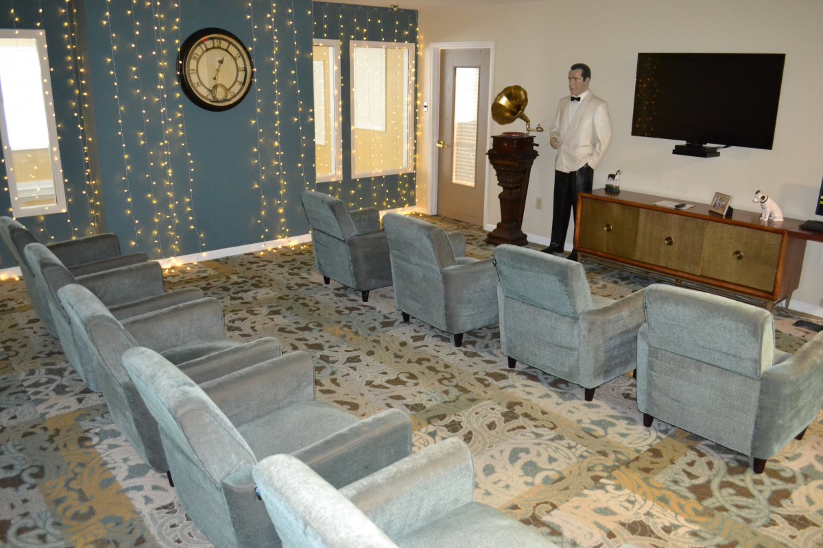 A retro-themed living room with multiple chairs facing a wall clock and gramophone.