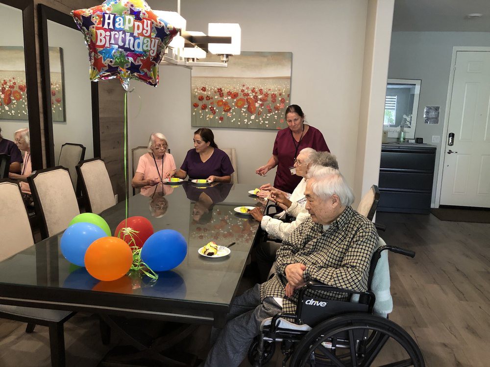 A birthday celebration with seniors gathered around a table decorated with balloons.