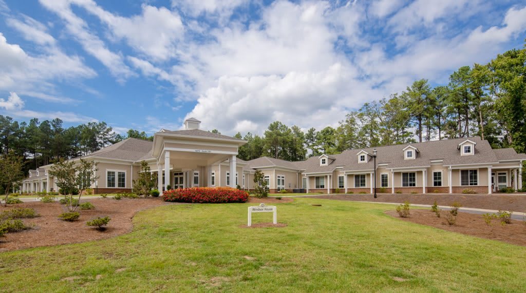 A large residential house with a spacious lawn and a cloudy sky in the background.