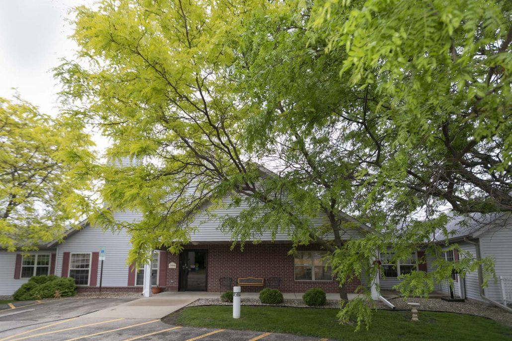 A small building surrounded by lush green trees and a parking area.