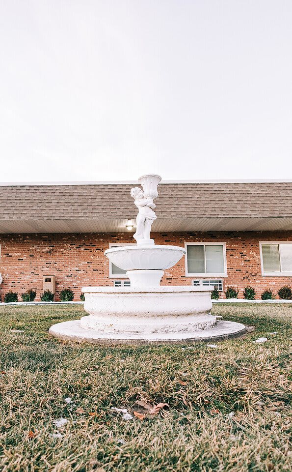 A decorative fountain with a statue stands in front of a brick building.