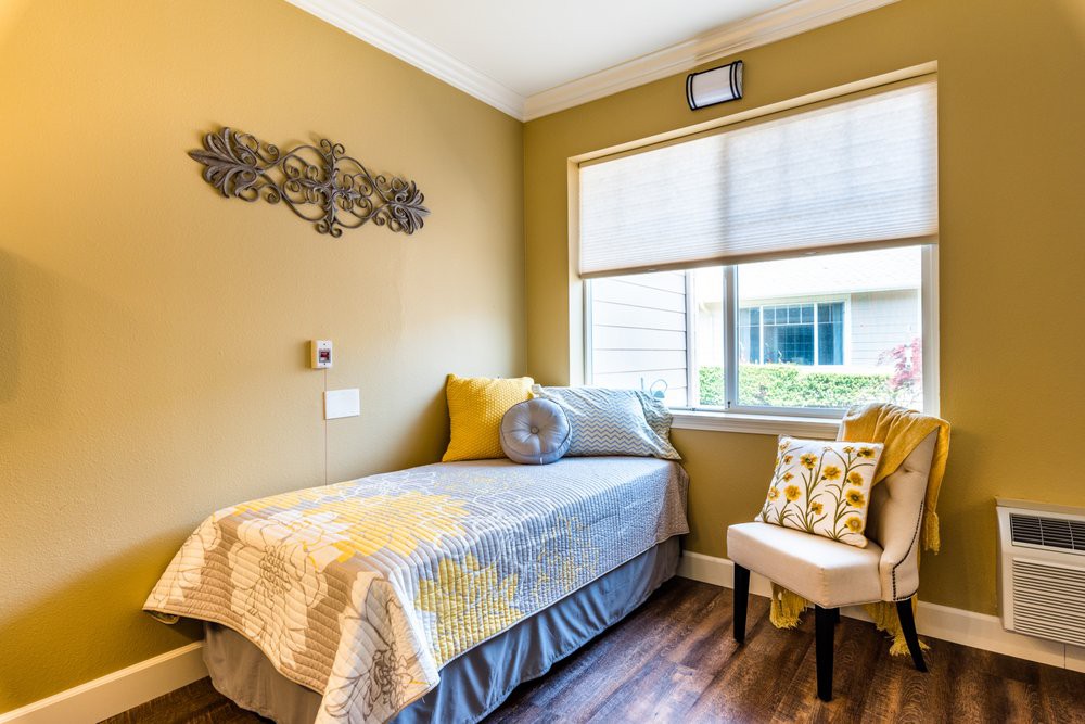 A cozy bedroom with a single bed, decorated pillows, and natural light streaming through the window.