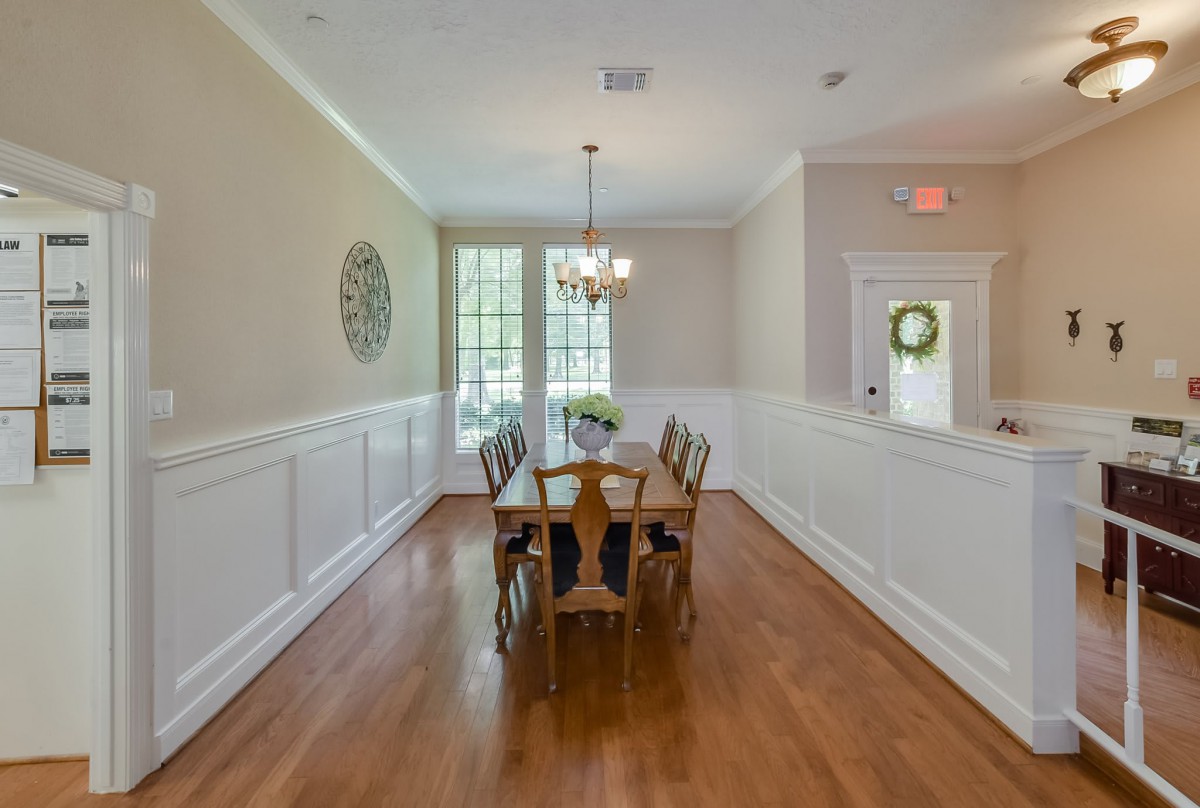 A bright dining room with a wooden table and chairs, featuring a chandelier and large windows.