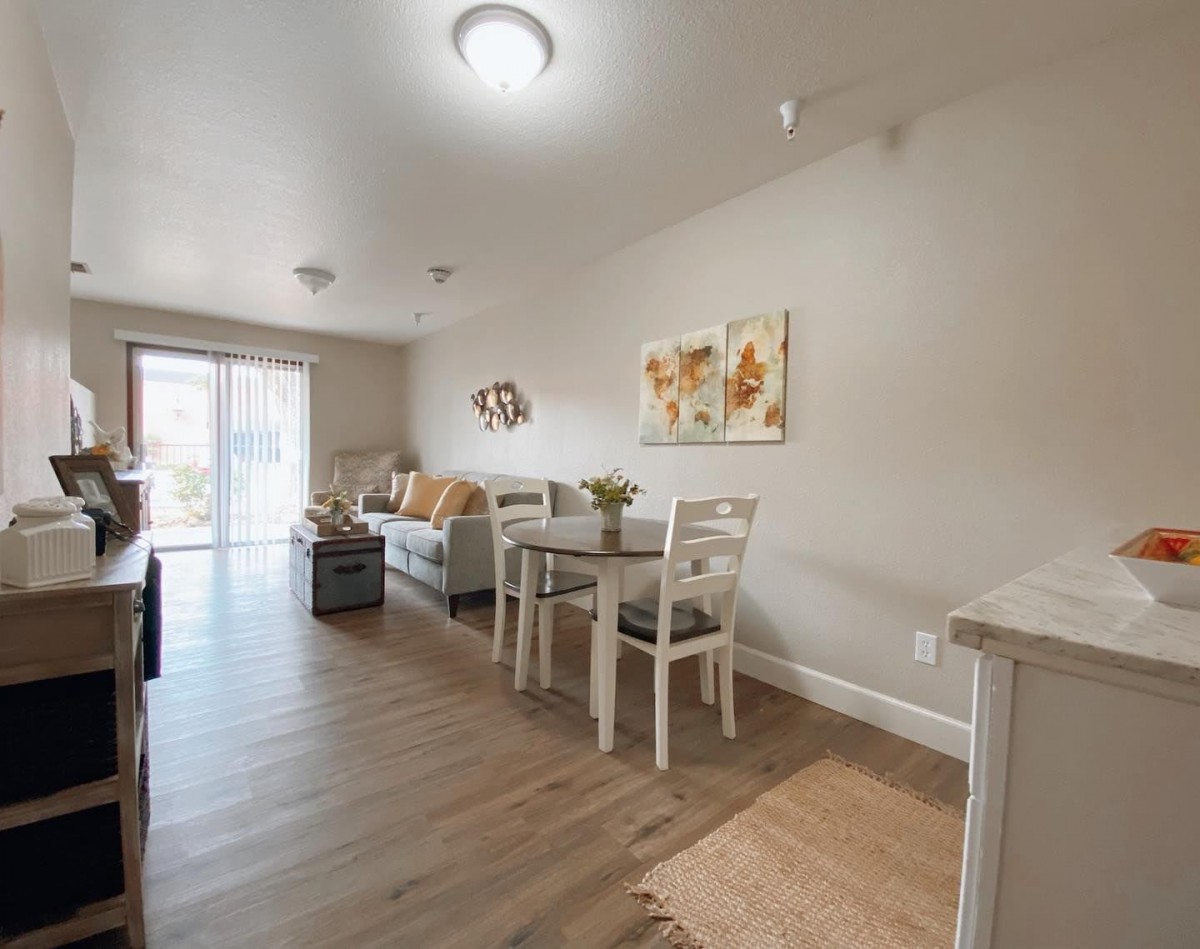 A modern apartment interior featuring a combined living and dining area with wooden flooring and contemporary furniture.