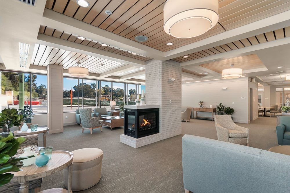 A modern lounge area with a central fireplace, comfortable seating, and large windows allowing natural light to fill the space.