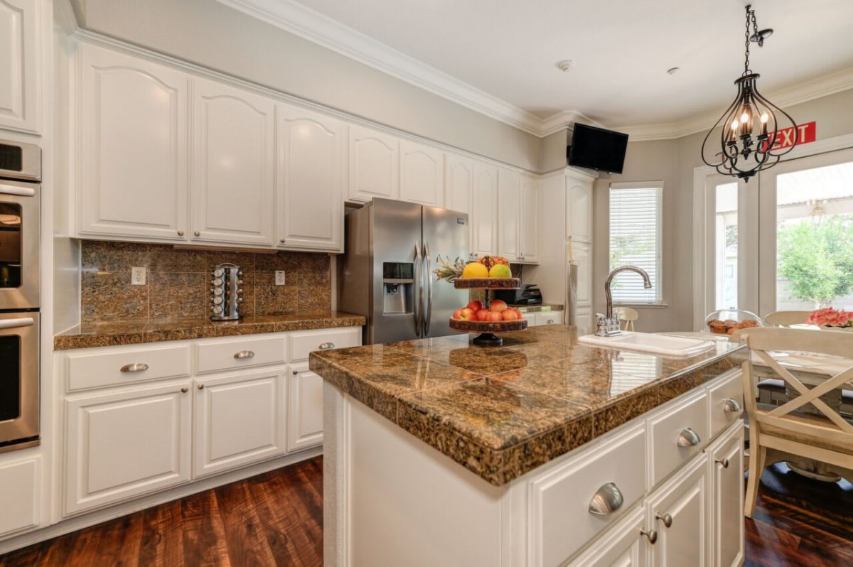 A modern kitchen featuring granite countertops, white cabinets, and stainless steel appliances.